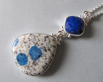 Könnte beinhalten: Eine silberne Halskette mit einem blauen Lapislazuli-Anhänger und einem tropfenförmigen Anhänger aus blau-weiß gesprenkeltem Stein.