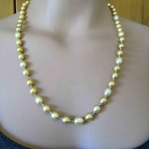 May include: A single strand necklace featuring round, lustrous golden-hued pearls. The pearls are strung together in a continuous line, displaying a smooth, reflective surface and a consistent warm yellow color throughout the entire length of the piece.