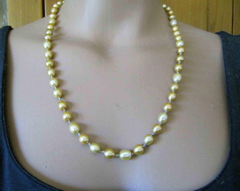 May include: A single strand necklace featuring round, lustrous golden-hued pearls. The pearls are strung together in a continuous line, displaying a smooth, reflective surface and a consistent warm yellow color throughout the entire length of the piece.