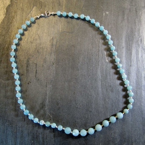 May include: A light blue gemstone necklace with a silver clasp. The necklace is made of round beads and is approximately 18 inches long.