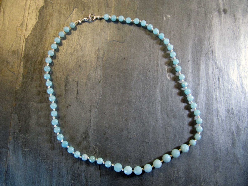 May include: A light blue gemstone necklace with a silver clasp. The necklace is made of round beads and is approximately 18 inches long.