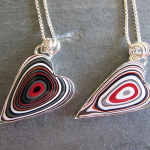 Puede incluir: Dos collares de plata con colgantes en forma de corazón. Los colgantes están hechos de ágata en capas con círculos concéntricos rojos, blancos y negros.