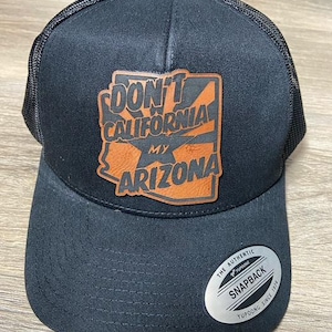 May include: Black and brown trucker hat with a leather patch that says "Don't California My Arizona". The hat has a mesh back and a YUPOONG SNAPBACK label.