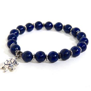 Könnte beinhalten: Ein blaues Lapislazuli-Perlenarmband mit einem silbernen Schildkrötenanhänger.