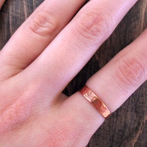 May include: A hammered copper ring on a finger. The ring is a simple band with a slightly rounded edge.