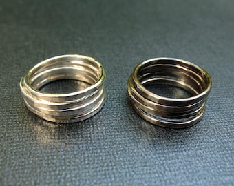 May include: Two silver rings, one with a smooth finish and the other with a hammered finish, are stacked on top of each other. The rings are both made of metal and have a shiny finish.