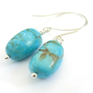 May include: A pair of silver dangle earrings with turquoise stones. The stones are a light blue color with brown veins.