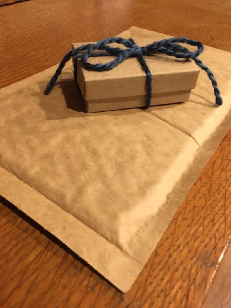 May include: A small, brown cardboard gift box tied with a dark blue twine bow, resting on a folded brown paper envelope. The items are on a wooden surface, creating a rustic aesthetic.