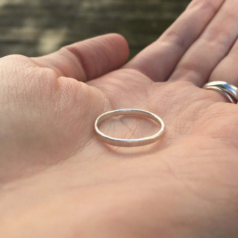May include: A simple silver band ring, shown on a person's palm.