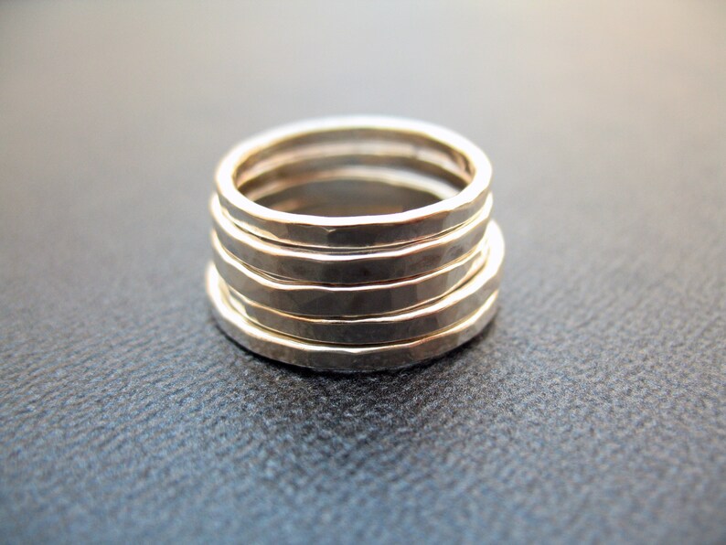 May include: Five silver rings stacked on top of each other. The rings are hammered and have a textured surface.