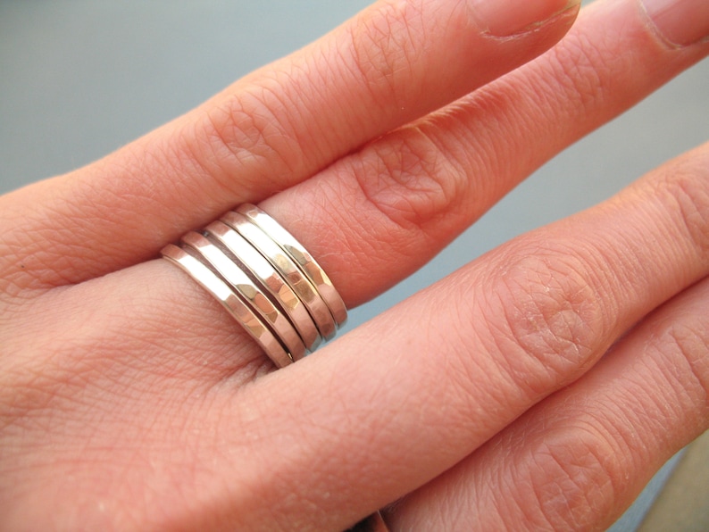 May include: A set of five silver hammered stacking rings. The rings are worn on a finger and are stacked on top of each other.