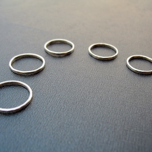 May include: Five silver rings of varying sizes arranged in a semi-circle on a gray surface.