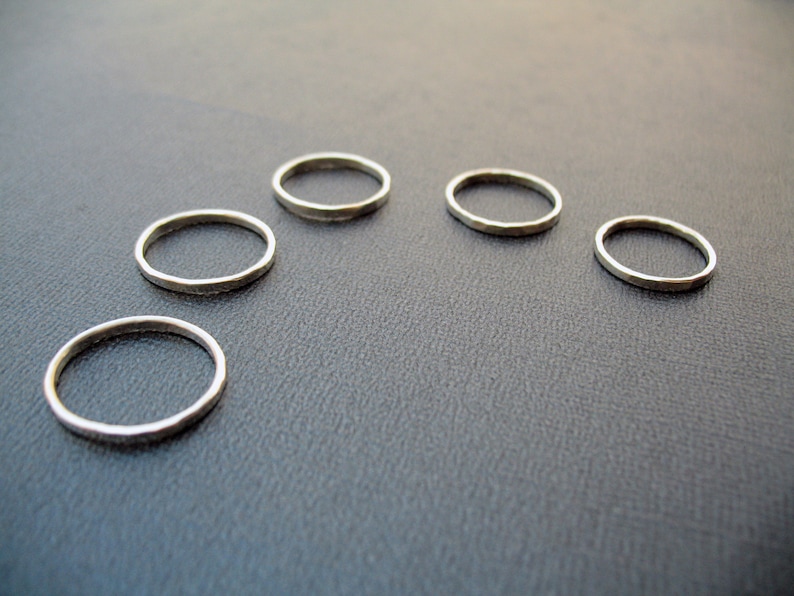 May include: Five silver rings of varying sizes arranged in a semi-circle on a gray surface.