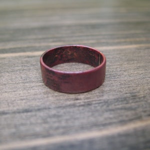 Könnte beinhalten: Ein einfacher, dunkelroter Ring aus Metall. Der Ring hat eine glatte, polierte Oberfläche.