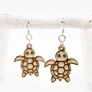 May include: A pair of wooden turtle earrings with a brown finish. The earrings are on a white background.