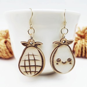 May include: A pair of wooden earrings featuring pear shapes. One earring has a grid pattern, and the other has a smiling face. The earrings are light brown with gold-colored hooks, perfect for adding a touch of whimsy to any outfit.