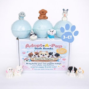 May include: A box of "Adopt-A-Pup" bath bombs with three light blue spheres, each topped with a small puppy figurine. The box features illustrations of puppies and text that reads "Puppies for Adoption!" and "3-CT".