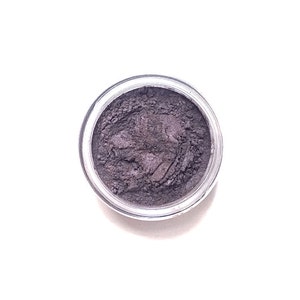 Pode incluir: Um pequeno frasco redondo cheio de pó de sombra para os olhos cinza escuro.