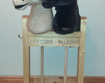 May include: A wooden stand with two plush horse heads, one brown and one tan, mounted on it. The stand has two wooden dowels and the words "POPCORN VALEGRO" are engraved on the front.