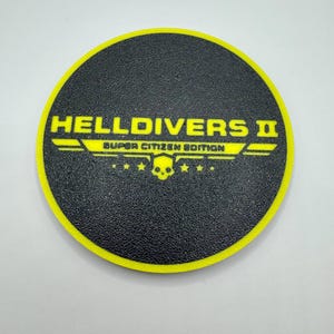 May include: A black and yellow round sticker with the text "HELLDIVERS II SUPER CITIZEN EDITION" and a skull graphic.