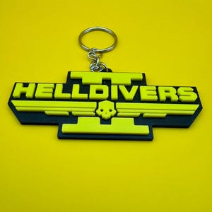 May include: A black and yellow 3D printed keychain with the text "HELLDIVERS II" and a skull logo.