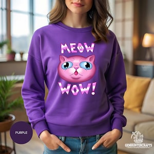 Può includere: Felpa viola con una grafica di un viso di gatto rosa e il testo "MEOW WOW!" stampato sul davanti.