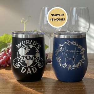 Op de afbeelding: Twee wijnglazen zonder voet. Eén zwarte beker heeft de tekst "WORLD'S GREATEST DAD" met een wereldbolafbeelding. De andere is marineblauw met "Hernandez Family" in een kransontwerp. De afbeelding bevat ook wijnglazen.