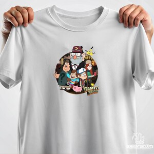 Może przedstawiać: Biała koszulka z nadrukiem graficznym postaci z serialu animowanego Gravity Falls. Postacie to Stan Pines, Dipper Pines, Mabel Pines, Wendy Corduroy i Soos Ramirez. Tekst "Gravity Falls" jest nadrukowany pod postaciami.