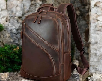 May include: A brown leather backpack with multiple zippered compartments and adjustable straps. The backpack has a distressed look and is made of high-quality leather.