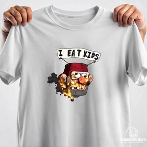 Puede incluir: Camiseta blanca con un personaje de dibujos animados en llamas con el texto "I EAT KIDS" sobre el personaje.