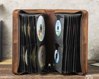 May include: A brown leather CD storage case with a zipper closure. The case is open and shows multiple slots for holding CDs. The case is made of genuine leather and has a rustic look.