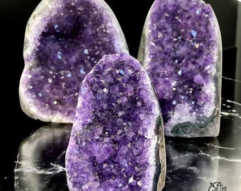 May include: Three amethyst crystal geodes, each with a unique shape and size. The geodes are filled with sparkling purple crystals.