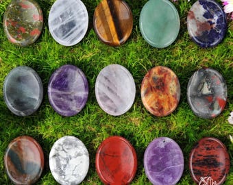 May include: Assortment of 16 polished gemstone palm stones in various colors and patterns, including amethyst, tiger's eye, green aventurine, and red jasper. The stones are arranged in a circle on a bed of green grass.