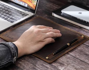 May include: A brown leather desk mat with a pen holder and a stitched border. The mat has the name "Charlotte" embossed on it.