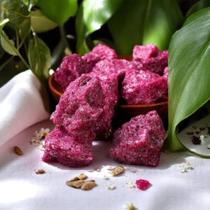 Op de afbeelding: Close-up van roze suikerkristallen in een bruine kom. De snoepjes zijn in een stapel gerangschikt en hebben een ruw, getextureerd oppervlak.