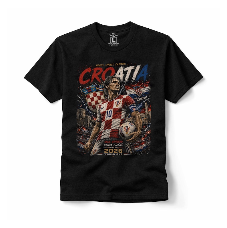 May include: A black short-sleeved t-shirt featuring a graphic print of a football player in a red and white chequered jersey holding a ball. The design includes the text "CROATIA", "2026 WORLD CUP", and other Croatian phrases, set against a stadium background.
