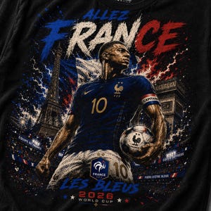 May include: A black t-shirt featuring a graphic of a football player in a blue jersey with the number 10, holding a football. The design includes the Eiffel Tower, the Arc de Triomphe, the text Allez France, Les Bleus, and 2026 World Cup.