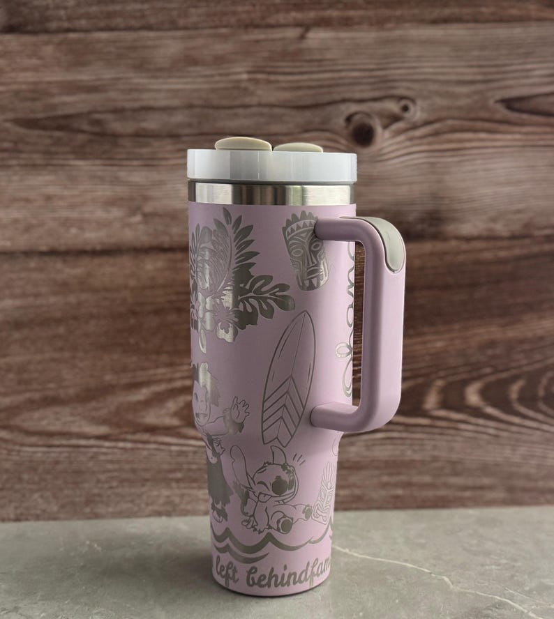 May include: A lavender stainless steel travel mug with a handle. The mug has a white lid and a design featuring Stitch, a character from the Disney movie Lilo & Stitch, along with tropical flowers and a surfboard. The text "left behind fam" is printed on the bottom of the mug.