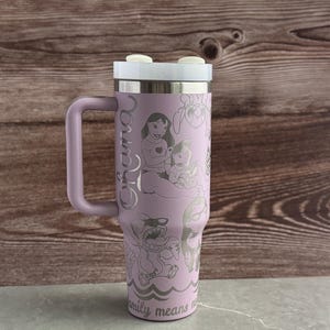 May include: A purple stainless steel travel mug with a handle. The mug has a white lid and is engraved with a design of Lilo and Stitch characters from the Disney movie Lilo & Stitch. The text "Ohana" is engraved on the side of the mug. The text "Family means no one gets left behind or forgotten" is engraved on the bottom of the mug.