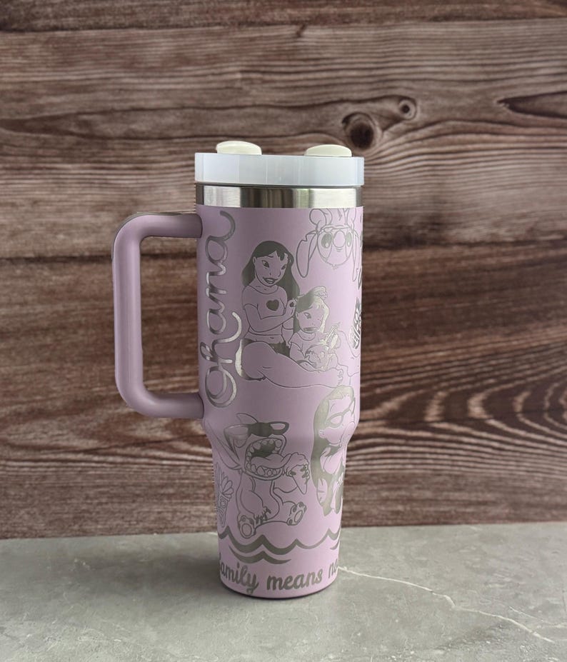 May include: A purple stainless steel travel mug with a handle. The mug has a white lid and is engraved with a design of Lilo and Stitch characters from the Disney movie Lilo & Stitch. The text "Ohana" is engraved on the side of the mug. The text "Family means no one gets left behind or forgotten" is engraved on the bottom of the mug.