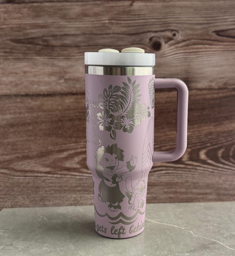 May include: A lavender stainless steel travel mug with a white lid and a handle. The mug has a design of Stitch and Lilo from the Disney movie Lilo & Stitch. The design is engraved on the mug and includes tropical flowers and leaves. The text "gets left behind" is at the bottom of the mug.