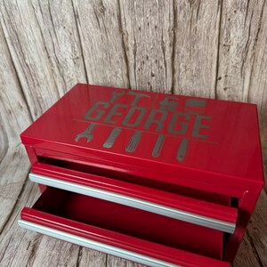 May include: Red metal toolbox with two drawers and a silver handle. The toolbox has the name "George" printed on the front in silver lettering with tool icons.