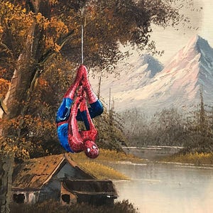Puede incluir: Una pintura de un paisaje con un lago, monta&ntilde;as y una caba&ntilde;a peque&ntilde;a. Una figura de superh&eacute;roe roja y azul est&aacute; colgada de una rama de &aacute;rbol.