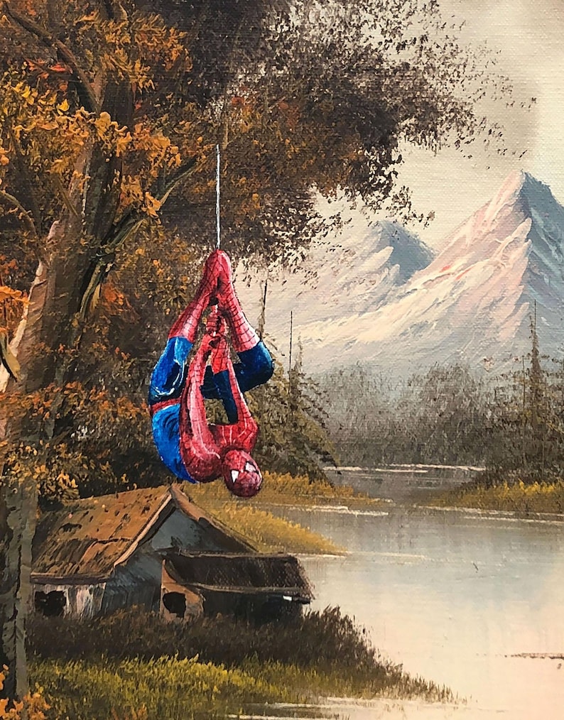 Puede incluir: Una pintura de un paisaje con un lago, monta&ntilde;as y una caba&ntilde;a peque&ntilde;a. Una figura de superh&eacute;roe roja y azul est&aacute; colgada de una rama de &aacute;rbol.