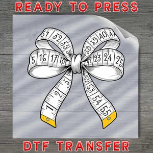 May include: A black and white illustration of a measuring tape shaped like a bow. The tape is marked with numbers and has yellow accents. The words "READY TO PRESS" and "DTF TRANSFER" are in red.