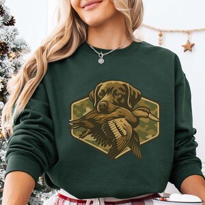 A woman wearing a green sweatshirt with a graphic of a dog holding a bird.