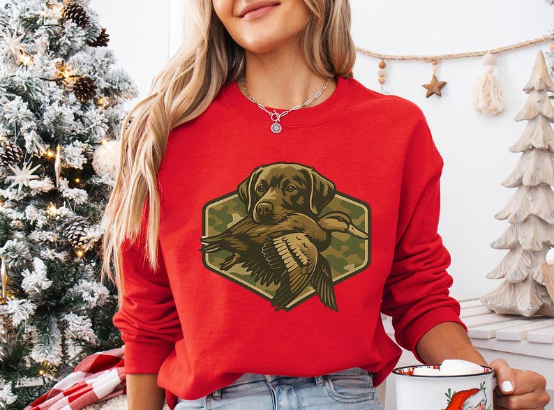 A woman wearing a red sweater with a graphic of a hunting dog holding a duck, standing in front of a Christmas tree.