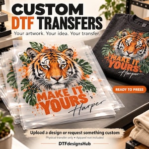 May include: A stack of clear DTF transfer sheets featuring a tiger head graphic surrounded by green monstera leaves and orange paint splatters. The text reads "MAKE IT YOURS Harper" in orange and black. A dark gray sweatshirt displays the same design.