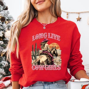 a woman wearing a red long sleeved shirt with a cowboy on it