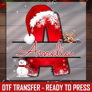 May include: A red letter "A" with a Santa hat and snowflakes, personalized with the name "Amelia" in red script. A reindeer and snowman are also featured. The text "DTF TRANSFER - READY TO PRESS" is at the bottom.